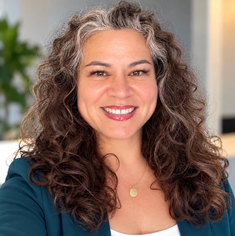 Belynda Ray smiling, with long curly hair, wearing a teal blazer